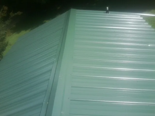 New green metal panels meeting at the ridge of a roof — Flat Roof Repair work by our crew in Ellendale
