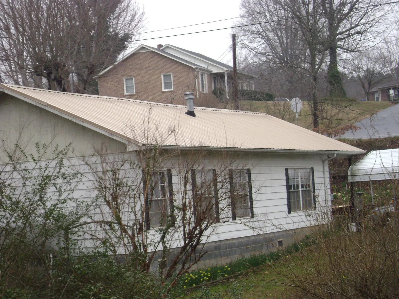 Tan metal roof on a white sided house set into a hillside — Commercial Roofing by Roofing Brothers in Ellendale